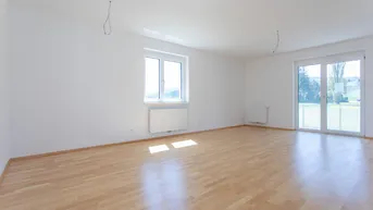 Helles, leeres Zimmer mit Parkettboden, weißen Wänden und Zugang zu einem Außenbereich.