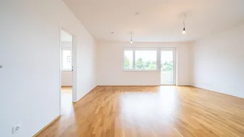 Lichtdurchfluteter Wohnbereich mit hellem Parkettboden und großem Fenster mit Blick ins Grüne.