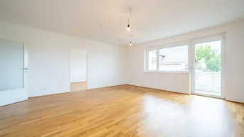 Helles, leeres Zimmer mit Parkettboden und Zugang zu einem Balkon, ideal als Wohnbereich.