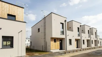 Moderne Reihenhäuser mit Flachdach, Holzverkleidung und Außentreppen für Dachzugang.