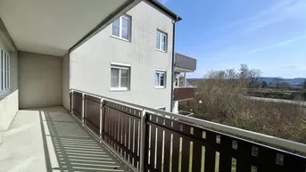 Langer Balkon mit braunem Geländer und Blick auf die umliegende Landschaft und Gebäude.