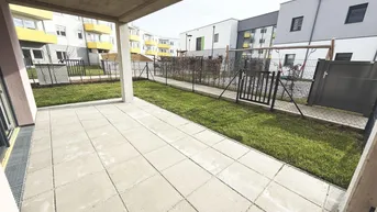 Große gepflasterte Terrasse mit Rasenfläche und Blick auf moderne Wohngebäude.