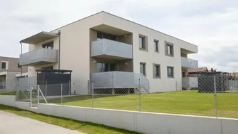 Modernes Mehrfamilienhaus mit beigefarbener Fassade, Balkonen und gepflegter Rasenfläche in ländlicher Umgebung.