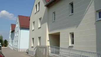 Mehrfamilienhaus mit heller Fassade, Satteldach und barrierefreiem Zugang über eine Rampe.