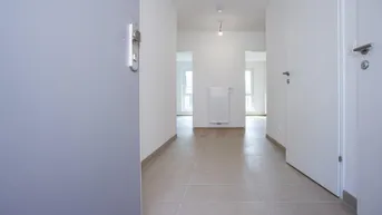 Heller Eingangsbereich mit Fliesenboden und Zugang zu verschiedenen Zimmern in einem Neubau.