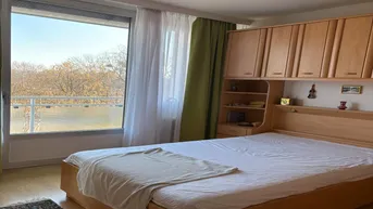 Helles Schlafzimmer mit Holzbett, Einbauschränken und Zugang zu einem Balkon mit Blick ins Grüne.