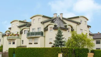 Mehrfamilienhaus mit gepflegter Fassade, Balkonen und grüner Hecke im Vorgarten.