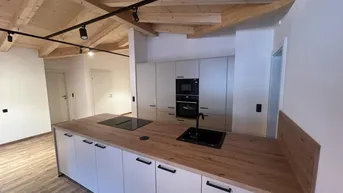 Moderne Küche mit Holzbalkendecke, Kücheninsel und integrierten Geräten in einem offenen Wohnbereich.