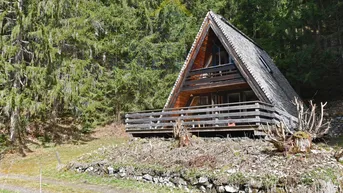 Rustikales A-Rahmen-Haus aus Holz mit Balkon, umgeben von dichtem Wald und Natur.
