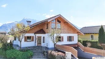Traditionelles Haus mit Holzfassade und Satteldach vor beeindruckender Bergkulisse.
