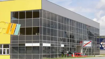 Modernes Gewerbegebäude mit auffälliger gelber Fassade und großer Glasfront, gut sichtbar von der Straße.