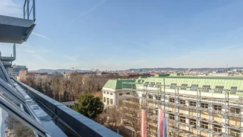 Weitblick über die Stadt von einem Balkon mit Gebäuden, Bäumen und blauem Himmel.