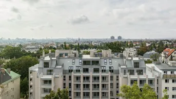 Luftaufnahme eines modernen Apartmentgebäudes mit Blick auf die Stadt und umliegende Grünflächen.