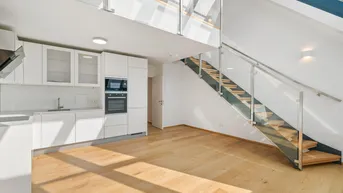 Helles, offenes Wohnzimmer mit integrierter Küche, Holzparkett und moderner Treppe zu einer Galerie.