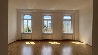 Helles, leeres Zimmer mit Parkettboden und drei hohen Bogenfenstern, die viel Tageslicht hereinlassen.
