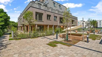 Modernes Wohngebäude mit Holzfassade und einem gemeinschaftlichen Gartenbereich mit Spielplatz.
