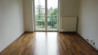 Leeres Zimmer mit Laminatboden und französischem Balkon, bietet Zugang ins Freie und grüne Aussicht.