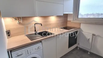 Moderne Einbauküche mit weißen Schränken, Holzarbeitsplatte und integrierter Waschmaschine.