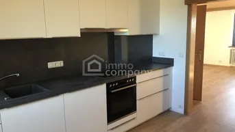 Moderne Einbauküche mit weißen Schränken, dunkler Arbeitsplatte und integriertem Backofen.