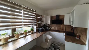 Moderne Küche mit weißen Schränken, Holzoptik-Arbeitsplatten und einem Fenster mit Jalousien.