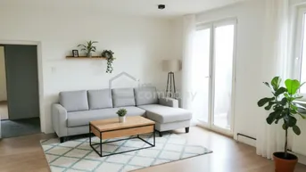 Helles Wohnzimmer mit modernem Sofa, Holzboden und Zugang zu einem Balkon oder einer Terrasse.