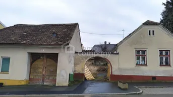 Alte Gebäude mit einem Torbogen, der zu einem Hinterhof führt, in ländlicher Umgebung.