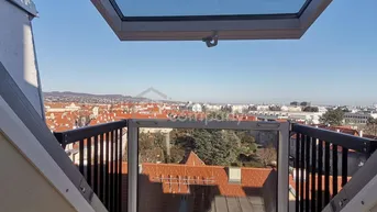 Weitblick über die Stadt mit roten Dächern und hügeliger Landschaft unter blauem Himmel von einem Dachfenster.
