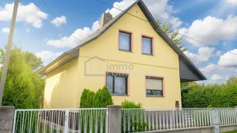 Gelbes Einfamilienhaus mit Satteldach, umgeben von einem gepflegten Garten und Zaun.