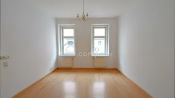 Leeres Zimmer mit hellem Parkettboden, weißen Wänden und zwei Fenstern, bereit zur Renovierung.