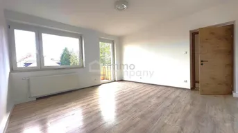 Heller Wohnraum mit Laminatboden, großen Fenstern und Zugang zu einem Außenbereich.
