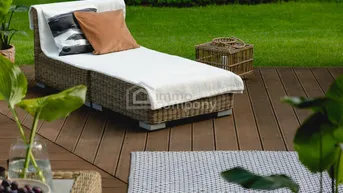 Gemütliche Sonnenliege auf einer Holzterrasse mit Blick ins Grüne und gepflegtem Rasen.