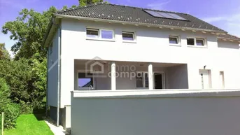Modernes Einfamilienhaus mit gepflegtem Vorgarten und Solarpaneelen auf dem Dach.