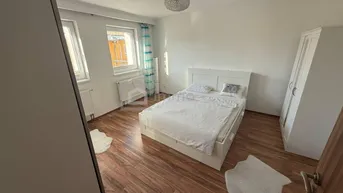 Schlafzimmer mit Laminatboden, Doppelbett und zwei Fenstern, die viel Tageslicht hereinlassen.