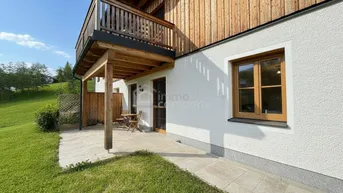 Kleine gepflasterte Terrasse mit Sitzgelegenheiten und Zugang zum Garten, umgeben von grüner Landschaft.