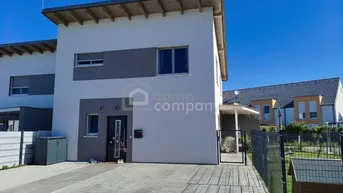 Moderne Doppelhaushälfte mit heller Fassade, gepflasterter Einfahrt und kleinem Vorgartenbereich.