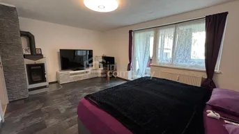 Schlafzimmer mit großem Bett, dunklem Fliesenboden und einem modernen Kaminofen neben dem Fenster.
