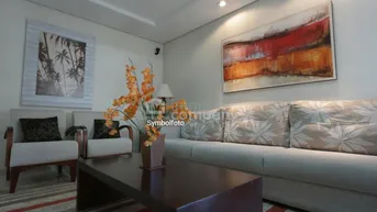 Gemütliches Wohnzimmer mit beigem Sofa, zwei Sesseln und einem dunklen Couchtisch, dekoriert mit Kunstwerken.