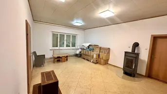 Geräumiger Raum mit einem Holzofen, Fliesenboden und einem Fenster, derzeit als Lager genutzt.