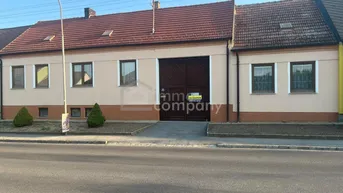 Altes Gebäude mit rotem Ziegeldach und großer Holztür, direkt an der Straße gelegen.