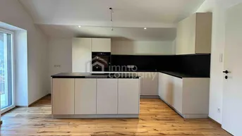 Moderne Küche mit weißer Kücheninsel, dunkler Arbeitsplatte und Holzboden, hell und geräumig.