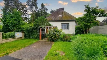 Kleines Einfamilienhaus mit Satteldach, umgeben von einem grünen Garten und Bäumen.