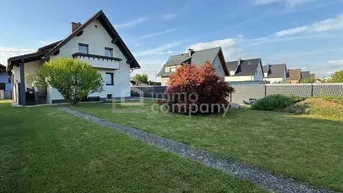 Großzügiger Gartenbereich mit Rasenfläche und Blick auf das moderne Einfamilienhaus bei Sonnenschein.