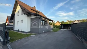 Modernes Einfamilienhaus mit gepflegtem Vorgarten und asphaltierter Auffahrt unter blauem Himmel.