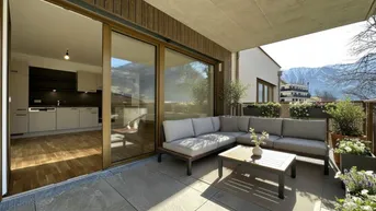 Geräumige Terrasse mit modernen Gartenmöbeln, Fliesenboden und Bergblick, offen zur Küche.