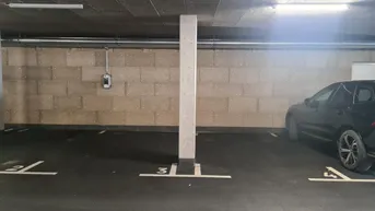 Tiefgarage mit markierten Stellplätzen, Betonwänden und einer Ladestation für Elektrofahrzeuge.