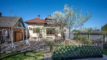 Gepflegter Gartenbereich mit Rasenfläche, Schaukel und blühenden Bäumen hinter dem Haus.