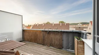 Möblierter Balkon mit Holzboden und Blick auf die umliegenden Wohngebäude.