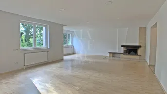 Helles Wohnzimmer mit Parkettboden, Kamin und Blick ins Grüne durch große Fenster.