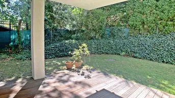 Überdachte Holzterrasse mit Blick auf den gepflegten Garten und die umliegende Hecke.