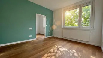 Helles Zimmer mit grüner Akzentwand, Holzboden und Blick ins Grüne durch das Fenster.